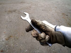 gloved hand of a maintenance technician holding a wrench gloved hand of a maintenance technician holding a wrench