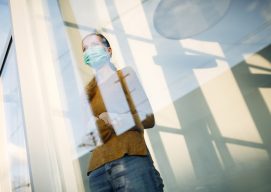mujer con mascarilla junto a la ventana