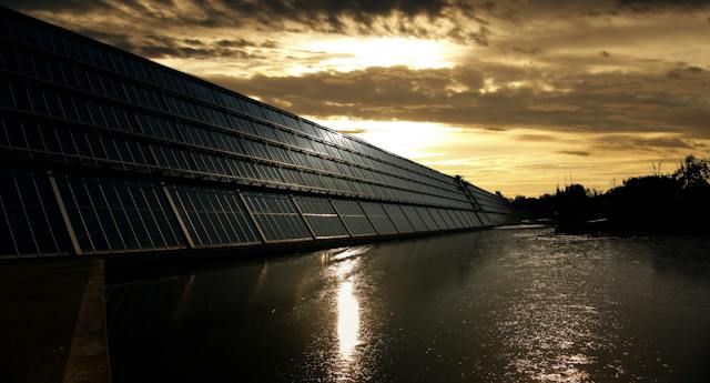 A large array of solar panels next to a body of water.