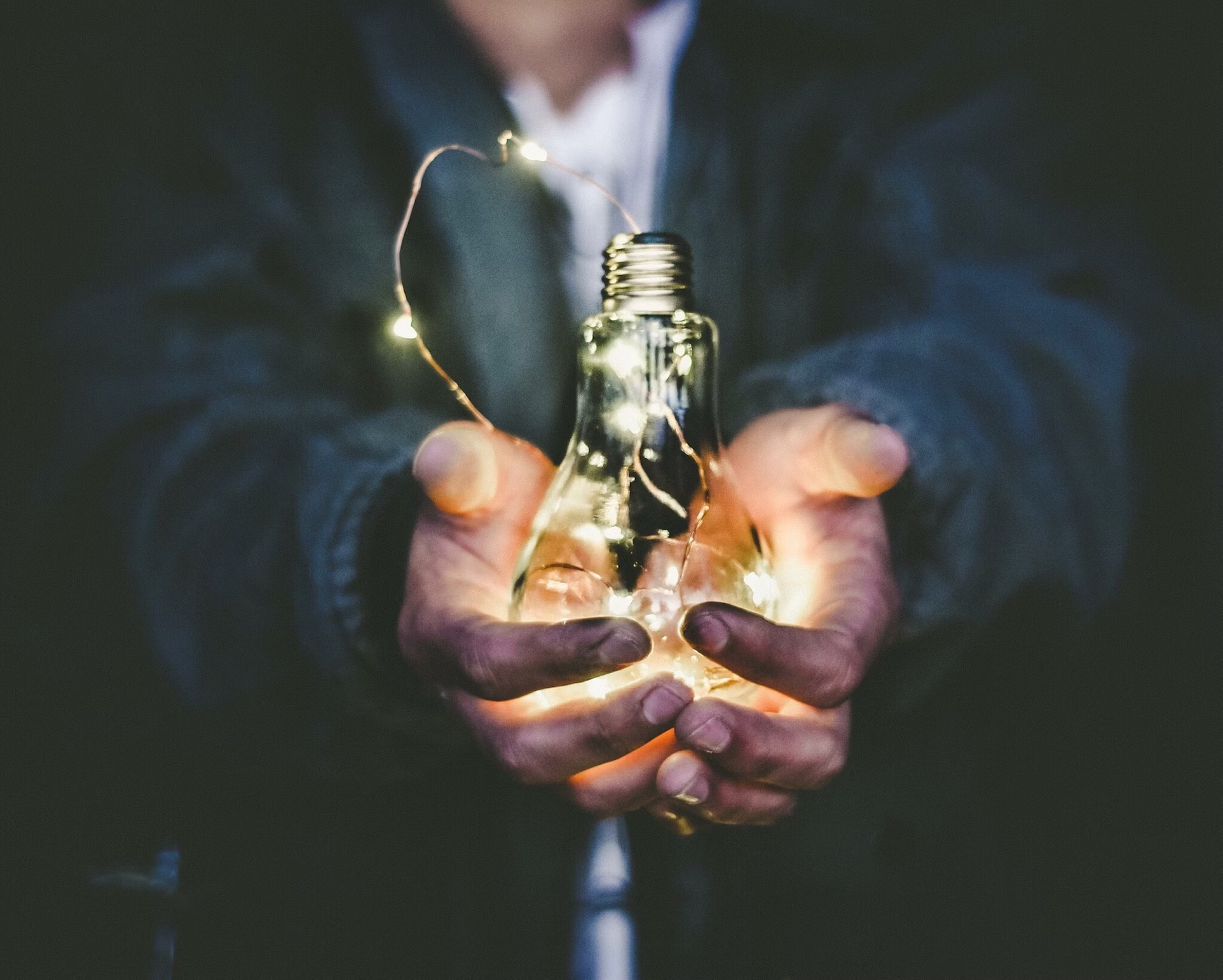 A man in a jacket holding a lit lightbulb 